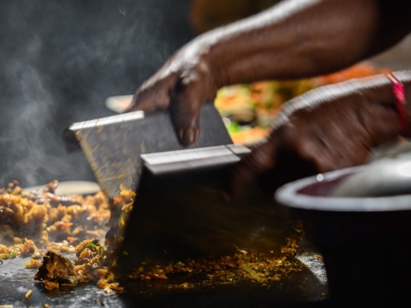 Kottu roti being prepared on a griddle with metal blades
